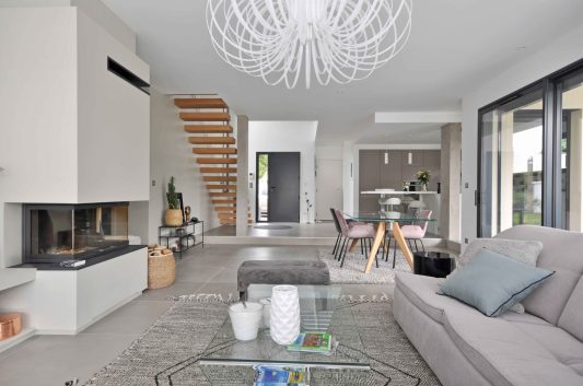 Aménagement de maison neuve de 170m² au nord-ouest de Lyon ; vue du salon ouvert avec cheminée vers escalier - PK intérieur, architecte d'intérieur